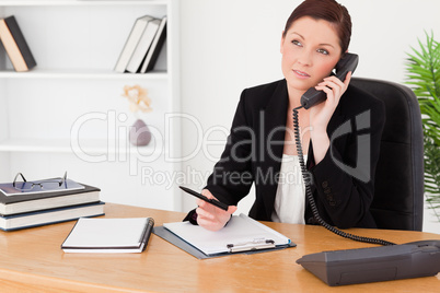 Good looking red-haired woman in suit writing on a notepad and p