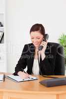 Young attractive red-haired woman in suit writing on a notepad a