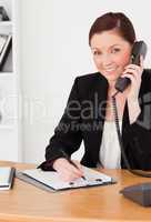 Young good looking red-haired woman in suit writing on a notepad