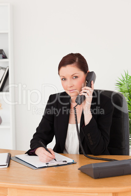 Young gorgeous red-haired woman in suit writing on a notepad and