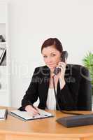 Young gorgeous red-haired woman in suit writing on a notepad and