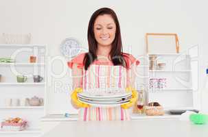Pretty red-haired woman posing while holding some dirty plates i