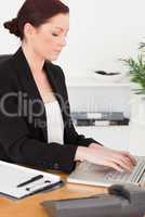 Young attractive red-haired woman in suit typing on her laptop