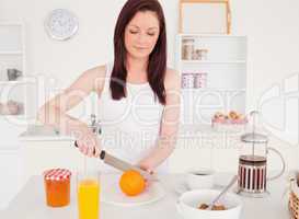Young good looking red-haired woman cutting an orange in the kit