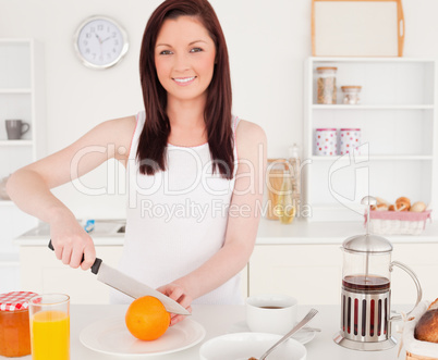 Young gorgeous red-haired woman cutting an orange in the kitchen