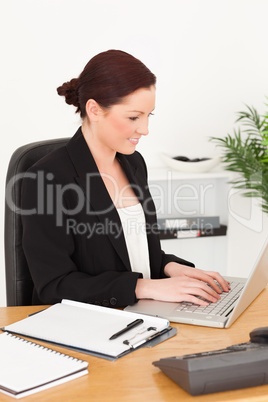 Young beautiful red-haired woman in suit typing on her laptop Young beautiful red-haired woman in suit typing on her laptop