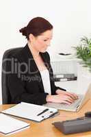 Young beautiful red-haired woman in suit typing on her laptop