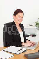 Young attractive red-haired woman in suit typing on her laptop a