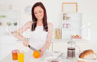Young beautiful red-haired woman cutting an orange in the kitche