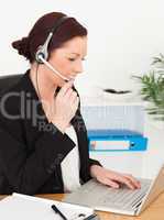 Young beautiful red-haired woman in suit typing on her laptop an