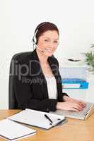 Young gorgeous red-haired woman in suit typing on her laptop and