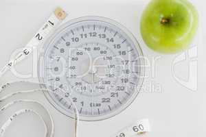 Top view of a green apple along with a tape measure and a weigh-