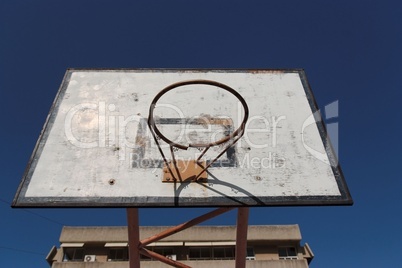 Old broken basketball hoop in the courtyard playground against the blue sky