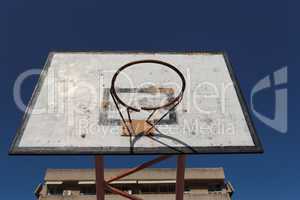 Old broken basketball hoop in the courtyard playground against the blue sky
