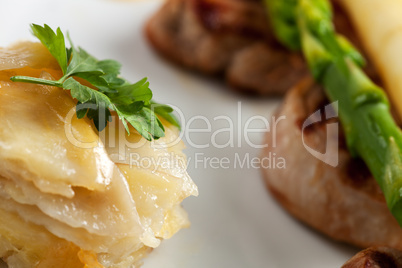 Nahaufnahme von Kartoffelgratin und weißem und grünem Spargel auf einer Scheibe Filet