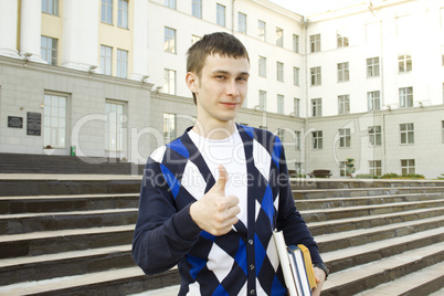 Male student on campus with textbooks. Thumbs up