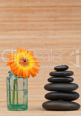 Orange snflower in a glass flask beside a black stones stack