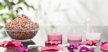 A bowl of brown gravel with pink petals and candles