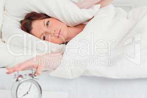 Charming red-haired woman waking up thanks to an alarm clock