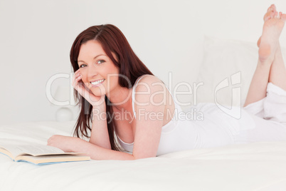 Good looking red-haired woman reading a book while lying on her