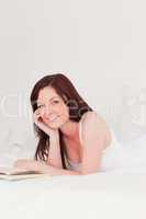 Charming red-haired woman reading a book while lying on her bed
