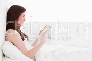 Pretty red-haired female reading a book while sitting on her bed