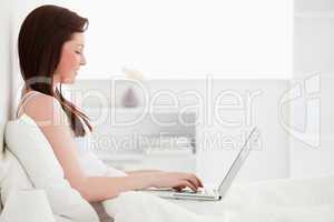 Attractive red-haired female relaxing with her laptop while sitt