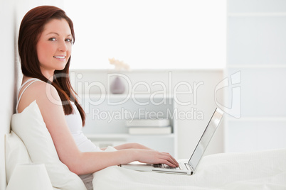 Beautiful red-haired female relaxing with her laptop while sitti