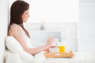 Cute red-haired female drinking a glass of orange juice while si