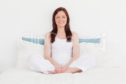 Good looking red-haired female relaxing while sitting on her bed