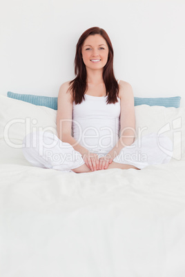 Pretty red-haired female relaxing while sitting on her bed