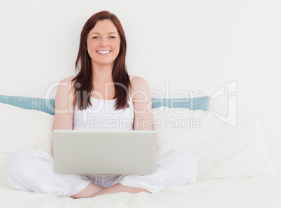 Pretty red-haired female relaxing with her laptop while sitting