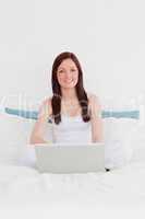 Beautiful red-haired woman relaxing with her laptop while sittin