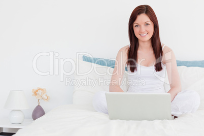 Attractive red-haired woman relaxing with her laptop while sitti