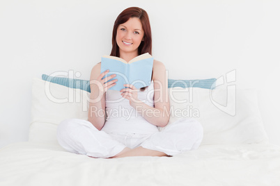 Gorgeous red-haired woman reading a book while sitting on her be
