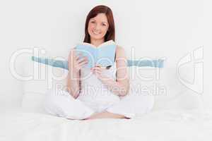 Gorgeous red-haired woman reading a book while sitting on her be