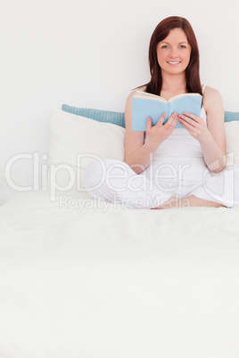 Charming red-haired woman reading a book while sitting on her be