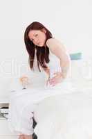 Attractive red-haired female posing while sitting on her bed