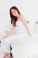 Good looking red-haired female posing while sitting on her bed