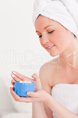 Beautiful young woman wrapped in a towel using skin cream
