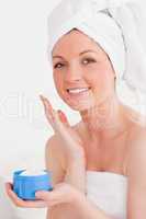 Charming young woman wrapped in a towel using skin cream