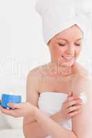 Cute young woman wearing a towel using skin cream