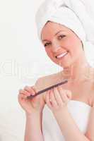 Attractive young woman wrapped in a towel using a nail file