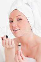 Beautiful young woman wearing a towel using a lip gloss