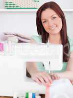 Attractive red-haired woman using a sewing machine in the living