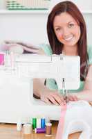 Charming red-haired woman using a sewing machine in the living r