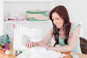 Pretty red-haired female using a sewing machine in the living ro
