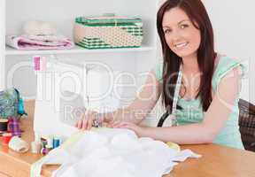 Attractive red-haired female using a sewing machine in the livin