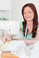 Beautiful red-haired female using a sewing machine in the living