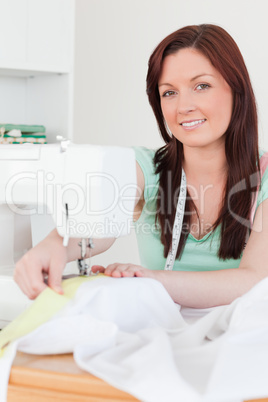 Gorgeous red-haired female using a sewing machine in the living